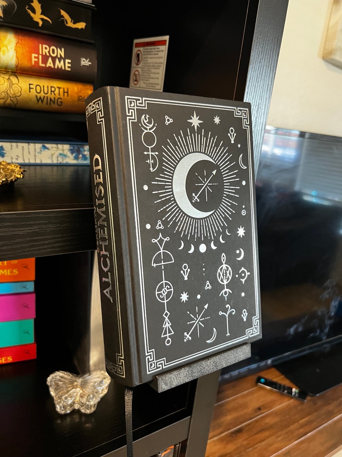 Black clamp-on book display holding a book in front of a bookshelf