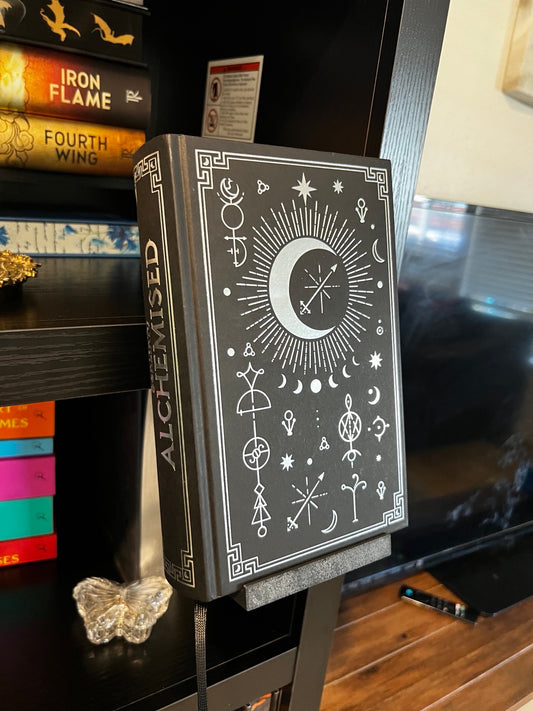 Black clamp-on book display holding a book in front of a bookshelf